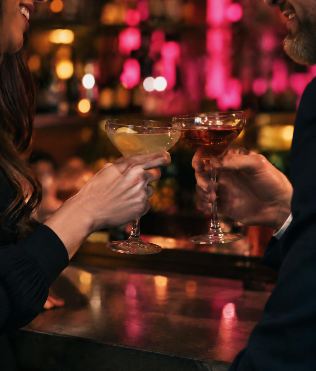Two people toasting cocktails at a bar